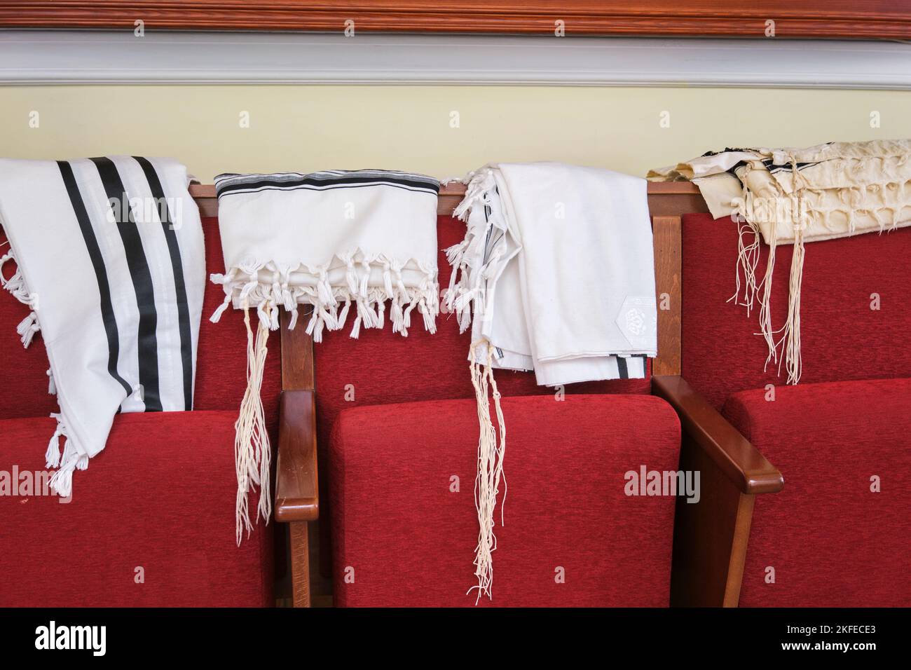 Quelques tallis, châles de prière tallite, pendent à l'arrière des chaises rouges à la synagogue blanche en bois Beit Rachel W Astanie. À Astana, Nur Sultan, Kazakh Banque D'Images
