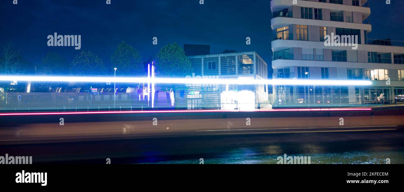 Des pistes lumineuses d'un bateau passant la nuit dans une ville avec quelques bâtiments en arrière-plan Banque D'Images
