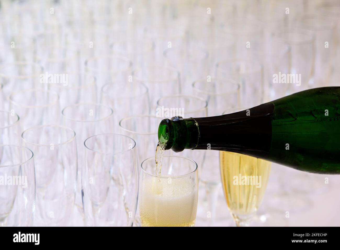gros plan d'une bouteille de champagne pooring du champagne dans une flûte de champagne contre des verres flous en arrière-plan Banque D'Images