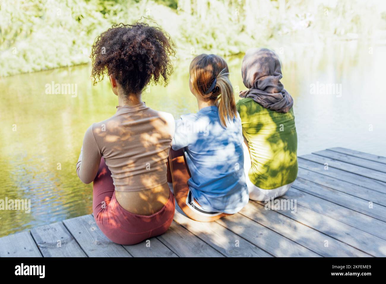 Vue arrière des jeunes adolescentes multiraciales qui se reposent dans le parc après un entraînement sportif et s'amusent ensemble. Diversité, sport et amitié c Banque D'Images