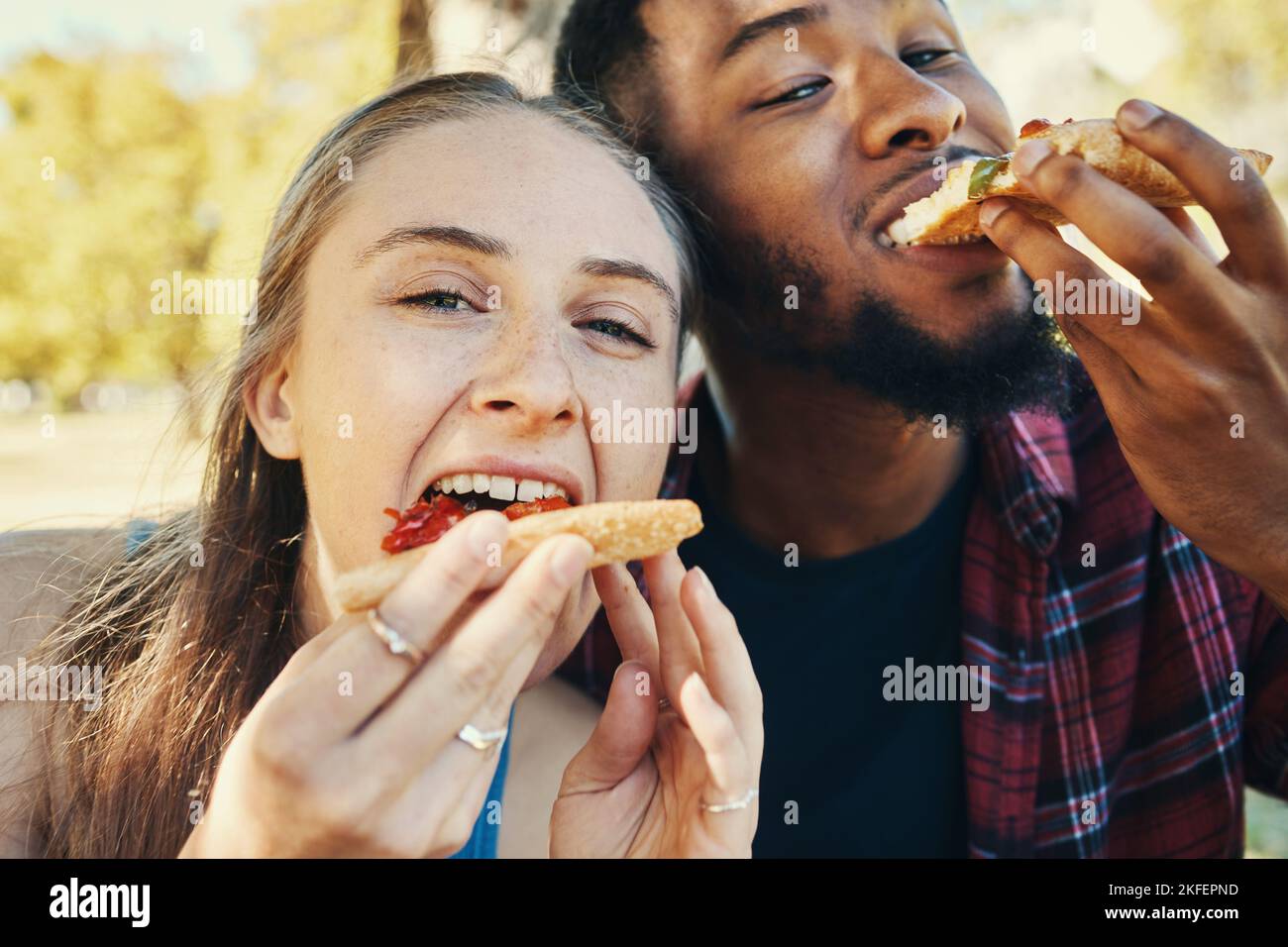 Pizza, amour et heureux couple de manger rapidement pendant un rendez-vous ensemble dans la nature dans un jardin. Faim, nourriture et portrait d'un homme et d'une femme interraciaux Banque D'Images