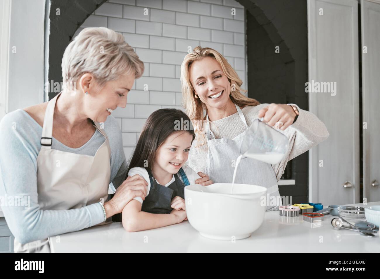 heureuse mère et fille cuisent ensemble dans la cuisine, utilisent  différents ingrédients, portent des tabliers, se tiennent contre  l'intérieur de la cuisine, la fille verse du lait à l'arc. maman  attentionnée apprend