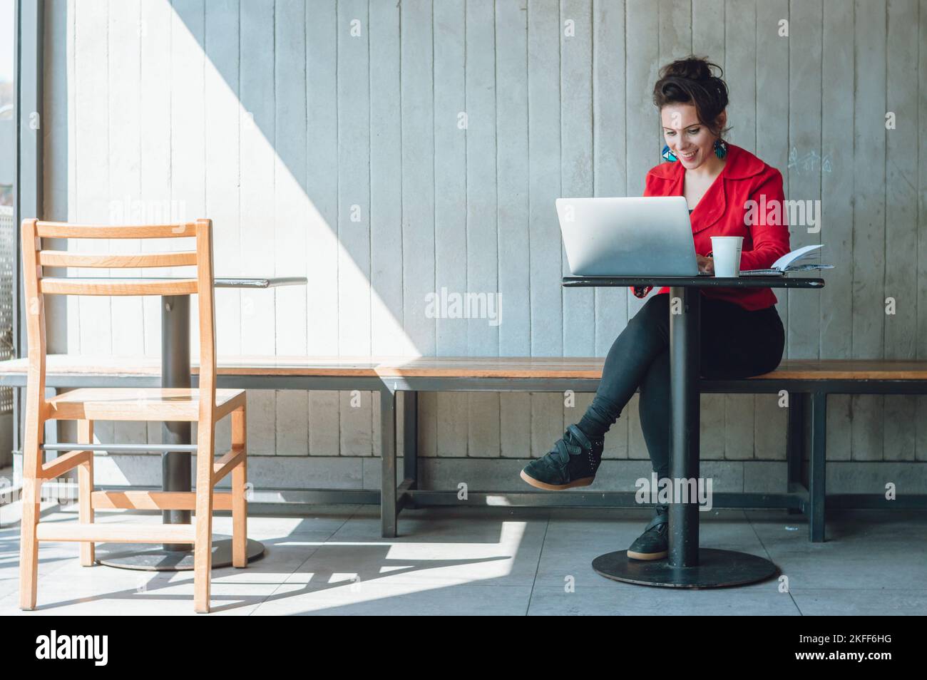 bonne femme d'affaires caucasienne adulte freelance portant un blazer rouge, assise à pieds croisés dans un café travaillant avec son ordinateur portable dans son entreprise numérique Banque D'Images