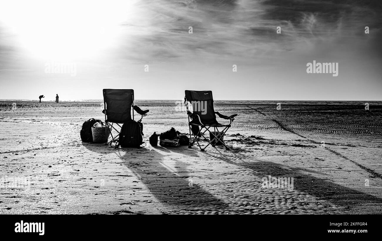 Image en noir et blanc de chaises de plage debout au premier plan sur une plage solitaire avec une séance photo en arrière-plan Banque D'Images