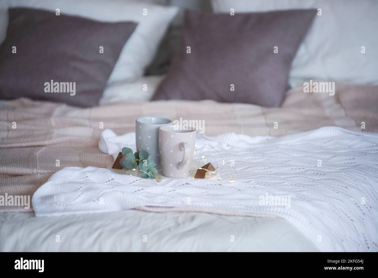 Sur un tissu tricoté, texturé, blanc, se trouve un plateau rond en marbre avec une branche d'eucalyptus vert, sur lequel il y a deux tasses grises avec des points de polka. Acquisition Banque D'Images