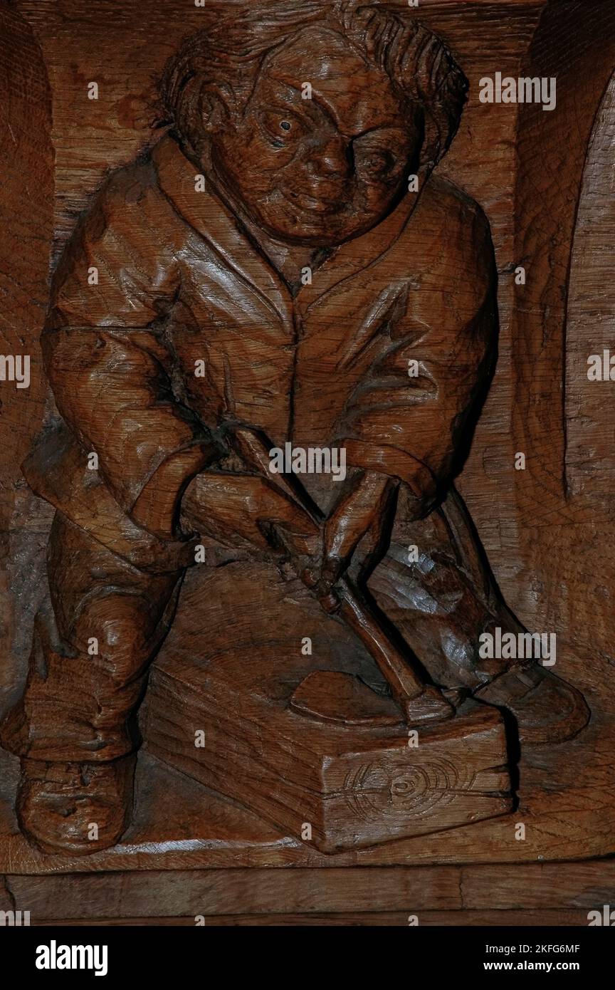 L'homme taille une botte de bois avec un adze. Sculpture sur bois moderne sur un miséricorde (dessous d'un siège basculant) dans l'un des stands de chœur de l'Oude Kerk (vieille église) à Oudekerksplein, Amsterdam, pays-Bas. La sculpture, achevée en 1974, est de Joop van Huisstede (1922-2000) et représente son fils, Jan Hop, ouvrier de mason, qui a travaillé avec van Huisstede à la restauration de l’église. Banque D'Images