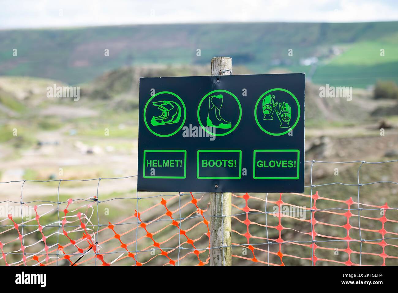Cowm Quarry Trails, Whitworth, Lancashire, Royaume-Uni. Panneau d'avertissement noir avec texte et bûches vert vif, casque, gants, bottes. Carrière en arrière-plan Banque D'Images