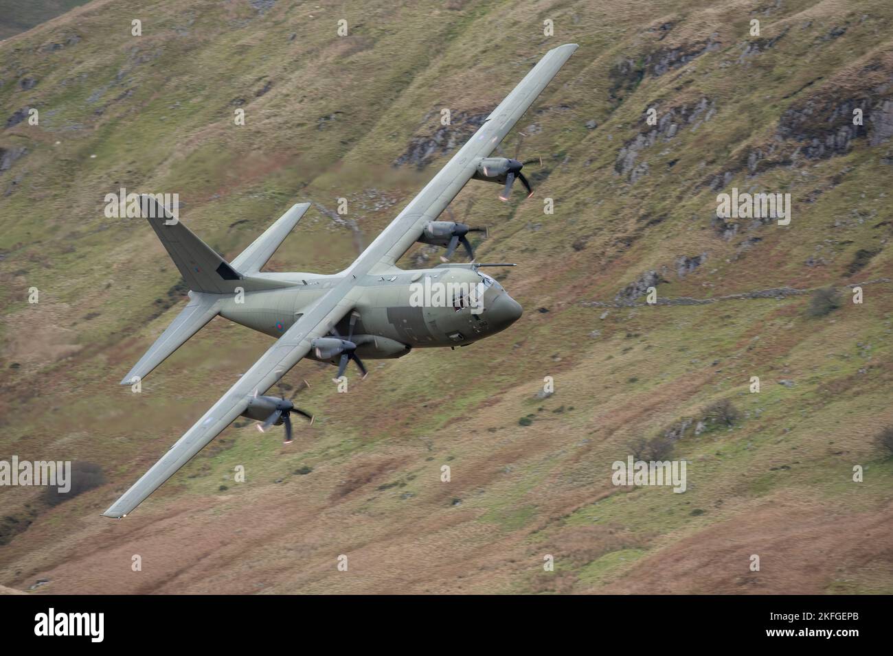 Machynlleth pays de Galles Royaume-Uni. RAF Hercules volant à travers la boucle Mach à bas niveau avec des collines et et des montagnes floues en arrière-plan Banque D'Images