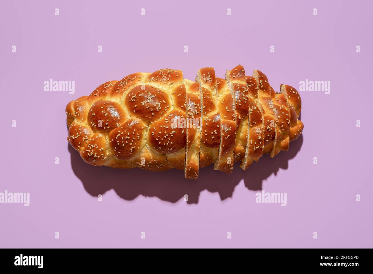 Vue ci-dessus avec un pain de challah maison minimaliste sur une table pourpre. Tranchez du pain dans une lumière vive sur un fond coloré. Banque D'Images