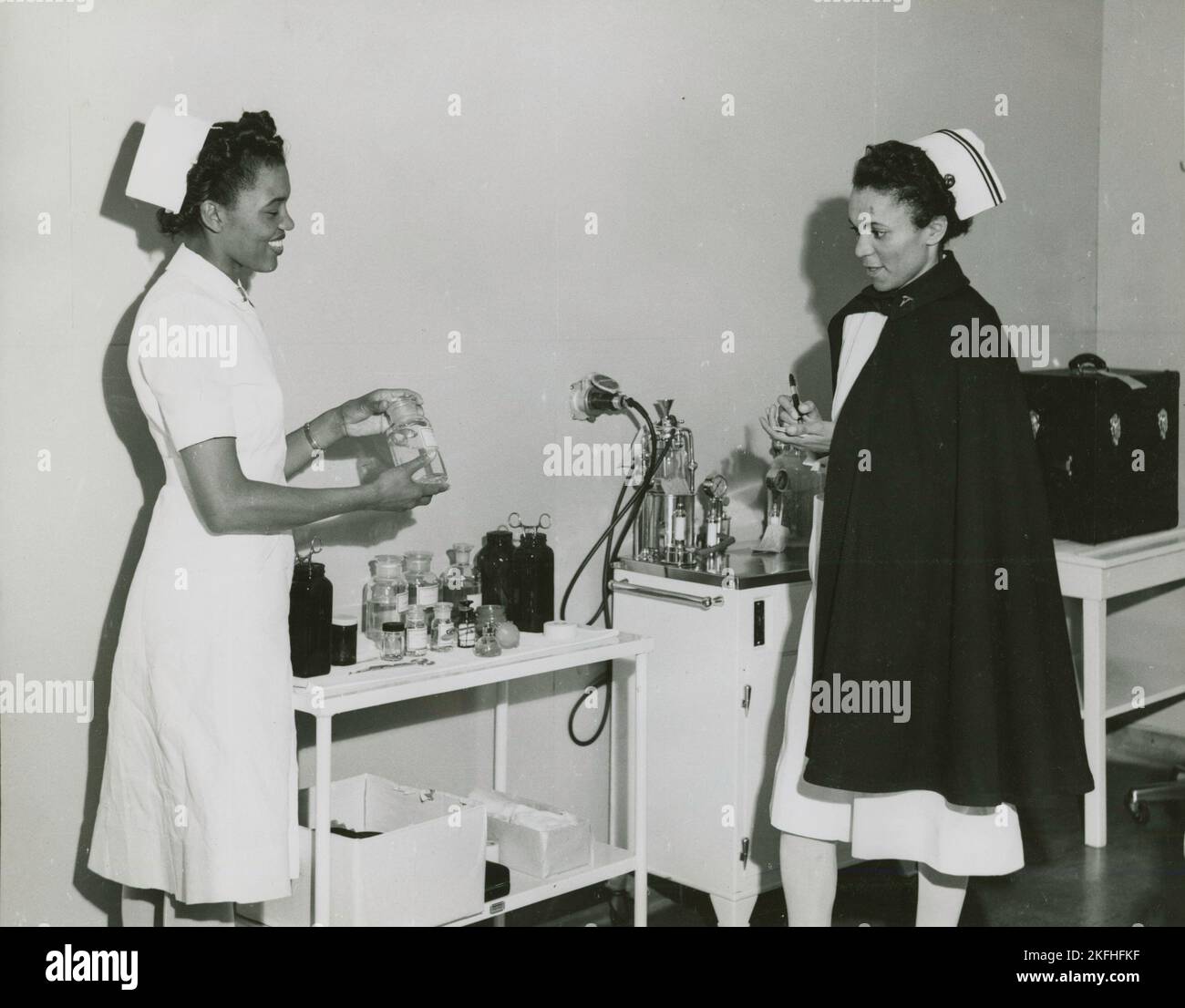 Capitaine Mary L. Petty, infirmière en chef, tenant une bouteille de verre et la montrant au 2nd Lieutenant Olive Bishop, qui écrit sur un petit bloc de papier, 1939 - 1945. Banque D'Images