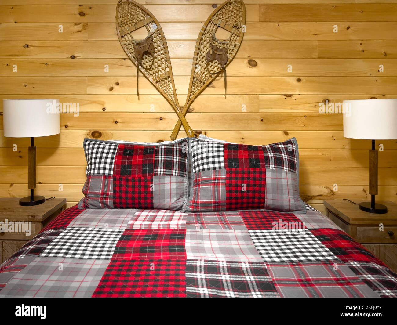 Oreillers avec draps sur le lit par des lampes électriques sur les tables de nuit et raquettes accrochées sur le mur en bois dans la cabine en rondins Banque D'Images