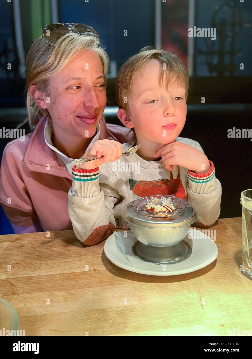 Une mère de race moyenne, de race blanche, souriante, regarde son mignon en train de manger un dessert rapide à la table du restaurant Banque D'Images