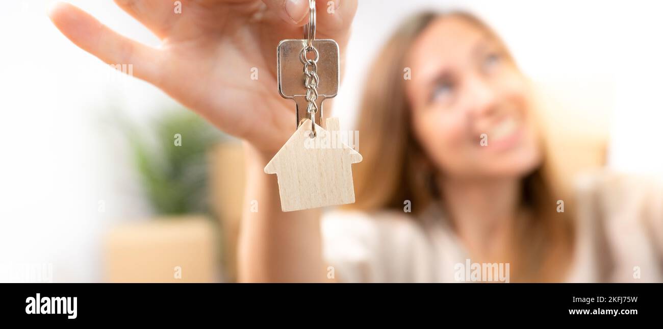 Bonne jeune femme souriant avec le nouveau porte-clés de la maison avec la maison en bois véritable bannière d'état Banque D'Images