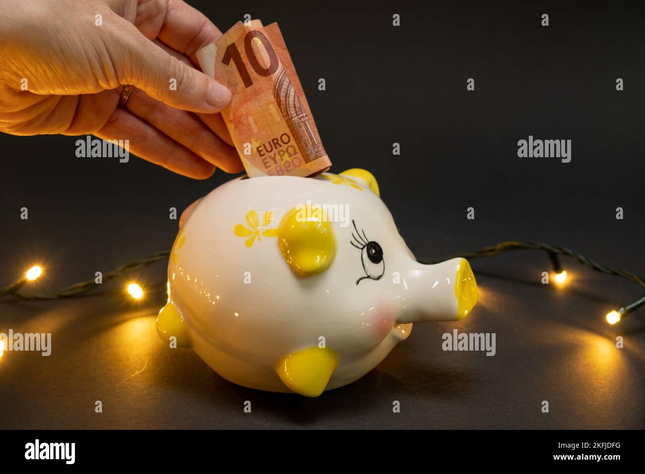 Mettre dix billets d'euros dans une banque de porc, sur un fond sombre avec des lumières à DEL. Vue latérale. Le concept de noël d'économiser de l'argent. copier l'espace. Banque D'Images