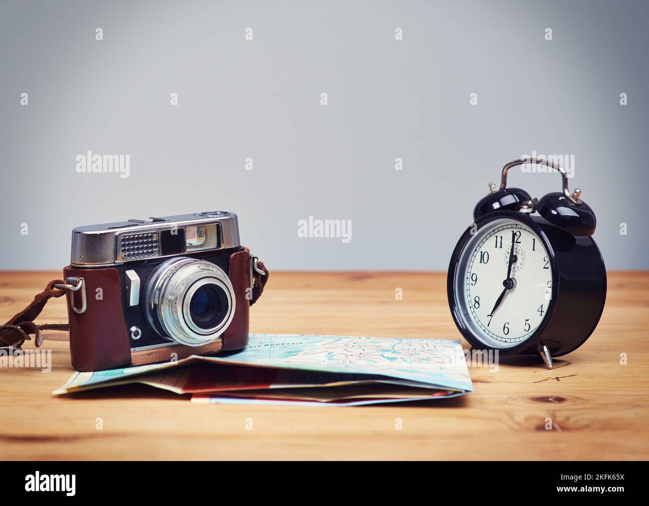 Montez et brillez le temps de partir à la découverte. Un appareil photo et une carte sont posés sur la table, à côté d'un réveil. Banque D'Images