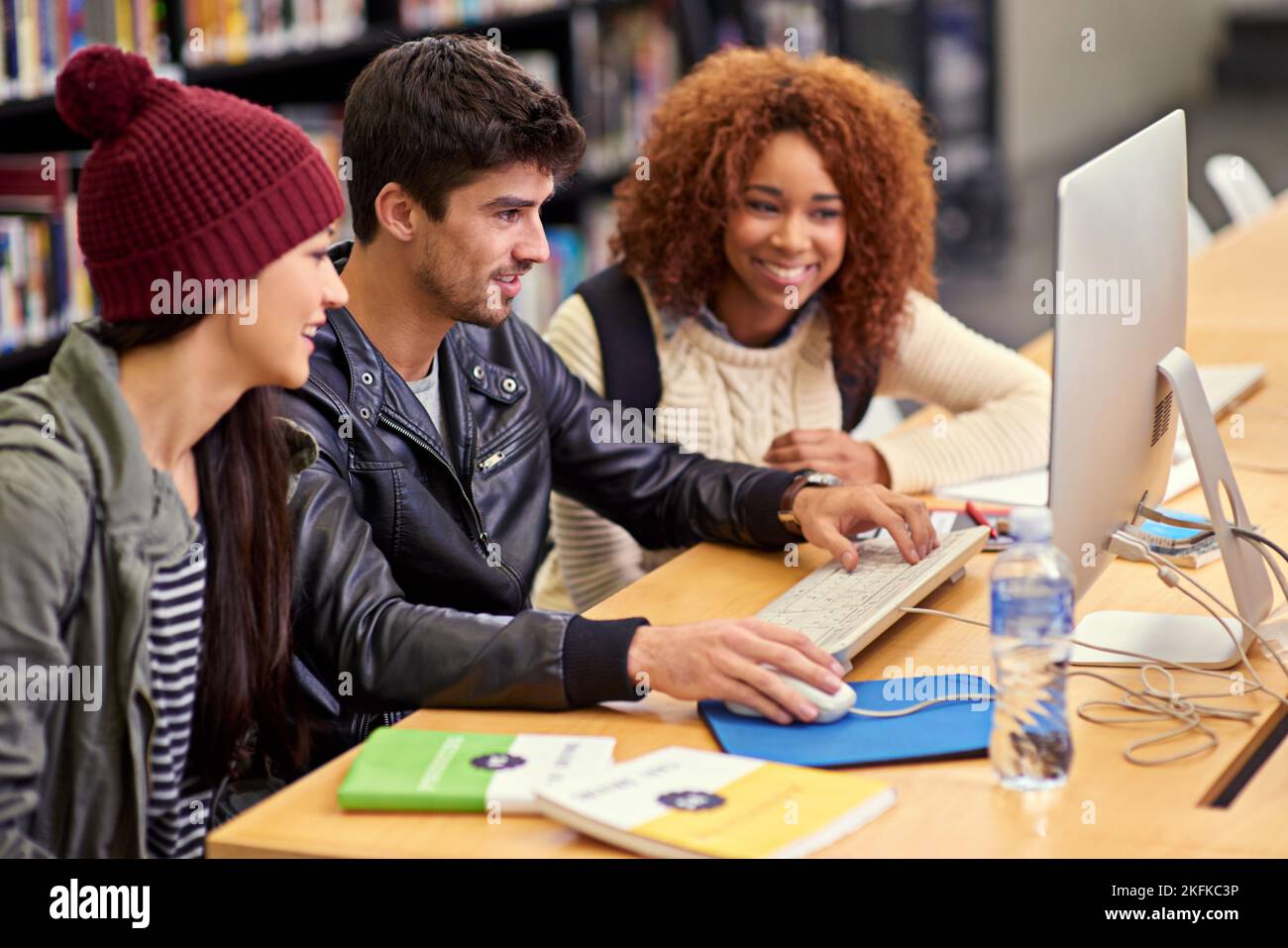En commençant par leur projet de recherche, un groupe d'étudiants travaillant ensemble à un ordinateur dans une bibliothèque universitaire. Banque D'Images