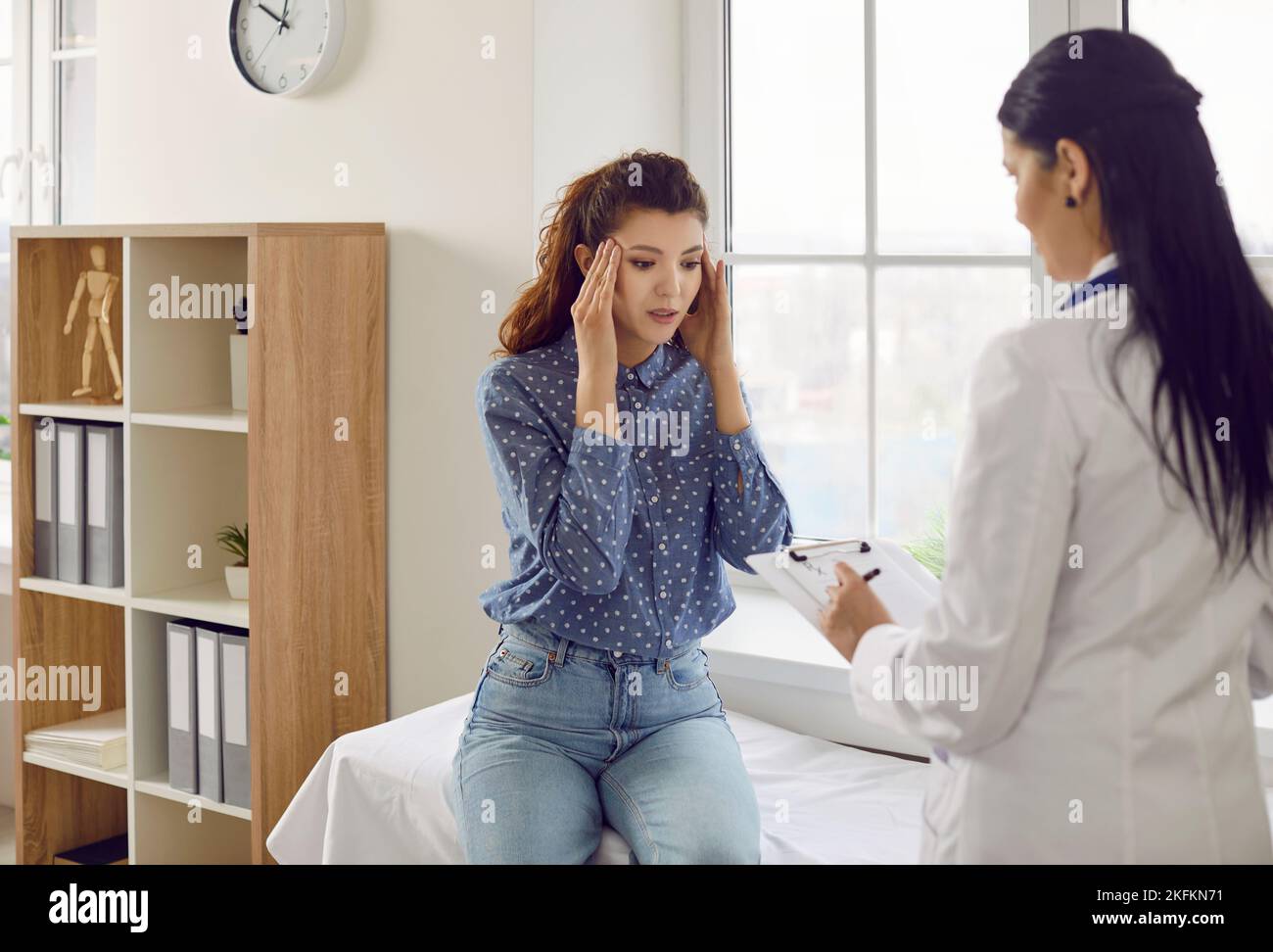 Jeune femme caucasienne au rendez-vous du médecin tenant la tête se plaignant de maux de tête ou de migraine Banque D'Images