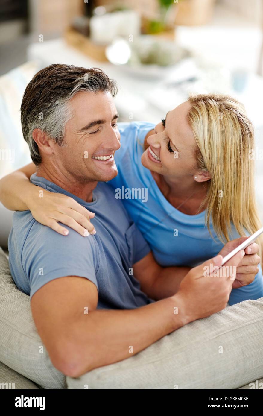 Nous avons toujours un rire ensemble. Un couple affectueux et mûr riant tout en utilisant une tablette numérique sur le canapé à la maison. Banque D'Images
