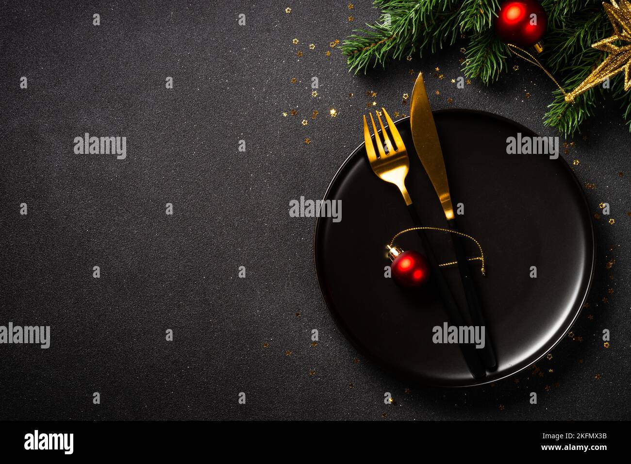 Table de Noël avec assiette noire, couverts dorés et décorations de Noël. Banque D'Images