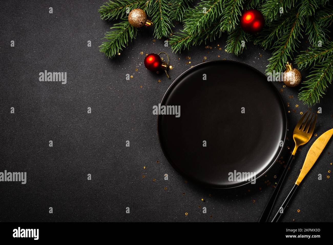 Table de Noël avec assiette noire, couverts dorés et décorations de Noël. Banque D'Images