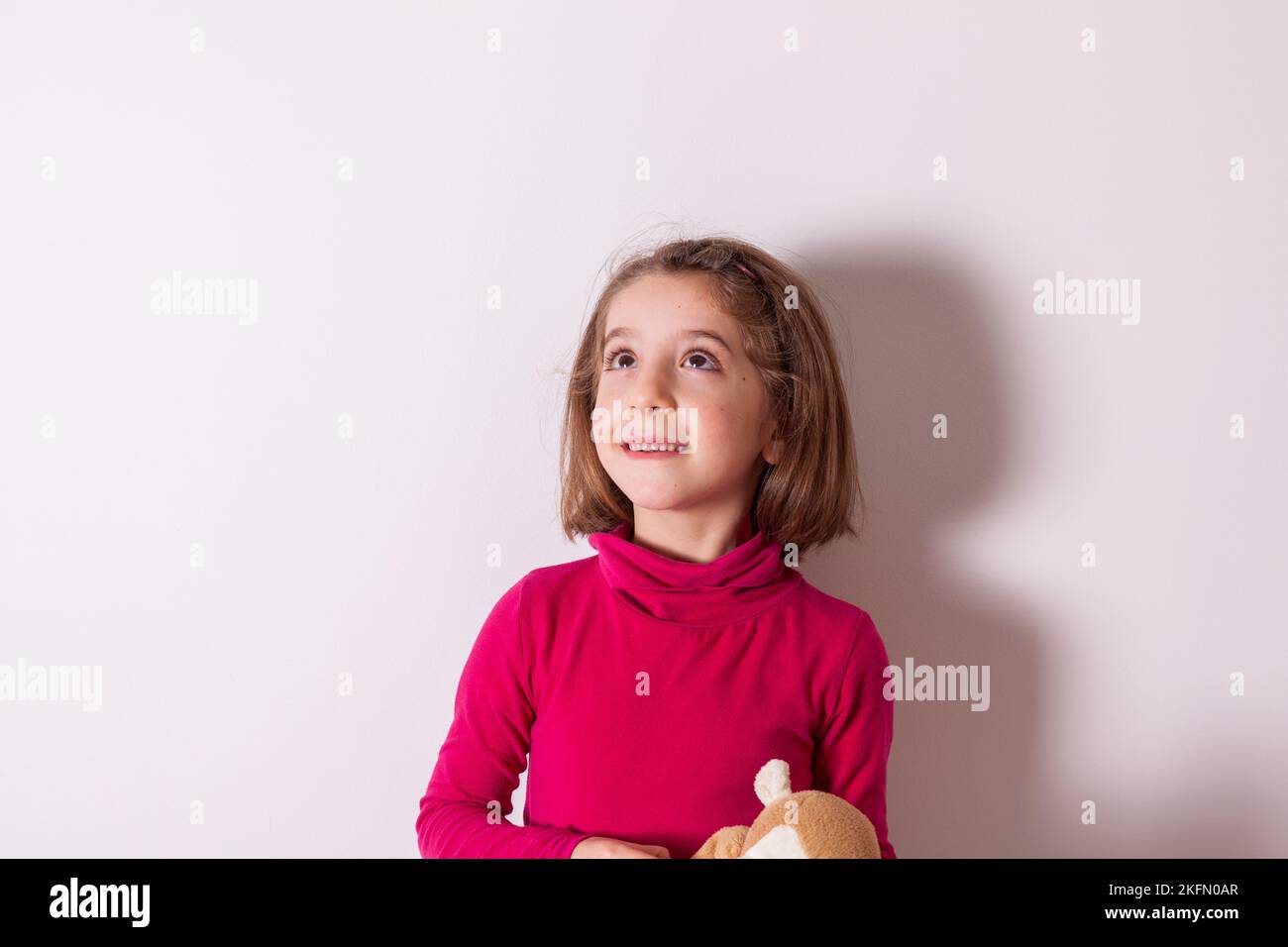 Petite fille portant un col polo ou un col roulé rouge souriant et regardant vers le haut sur fond blanc Banque D'Images