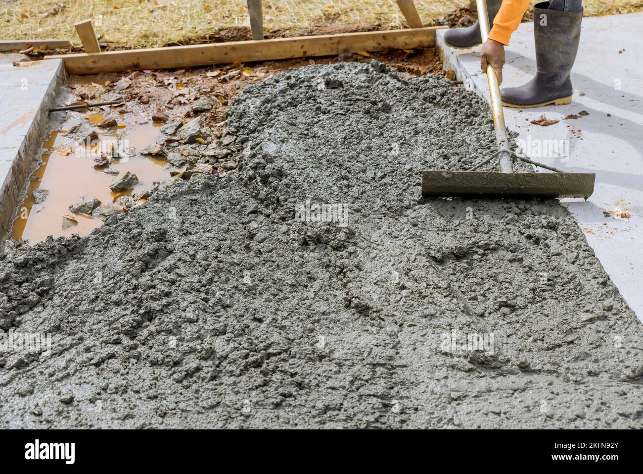 Le travailleur tient une truelle en acier pour lisser le sol sur un trottoir en béton fraîchement coulé dans la zone de construction Banque D'Images