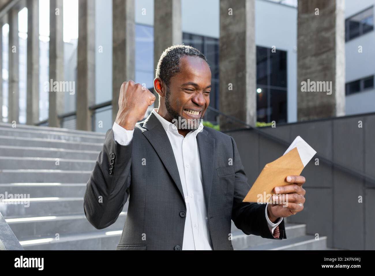 Un homme d'affaires afro-américain heureux a reçu une bonne lettre d'information, le patron dans le costume d'affaires lisant le document devant le bâtiment de bureau près des escaliers. Banque D'Images