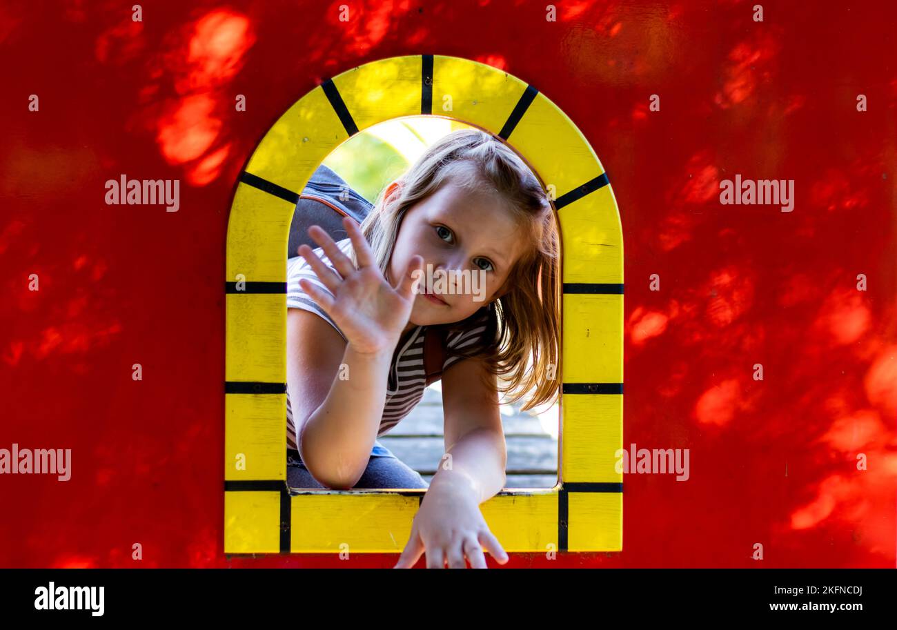 Le bébé joue sur l'aire de jeux. Une fille de 5 ans joue dans une maison de jouets rouges. Banque D'Images
