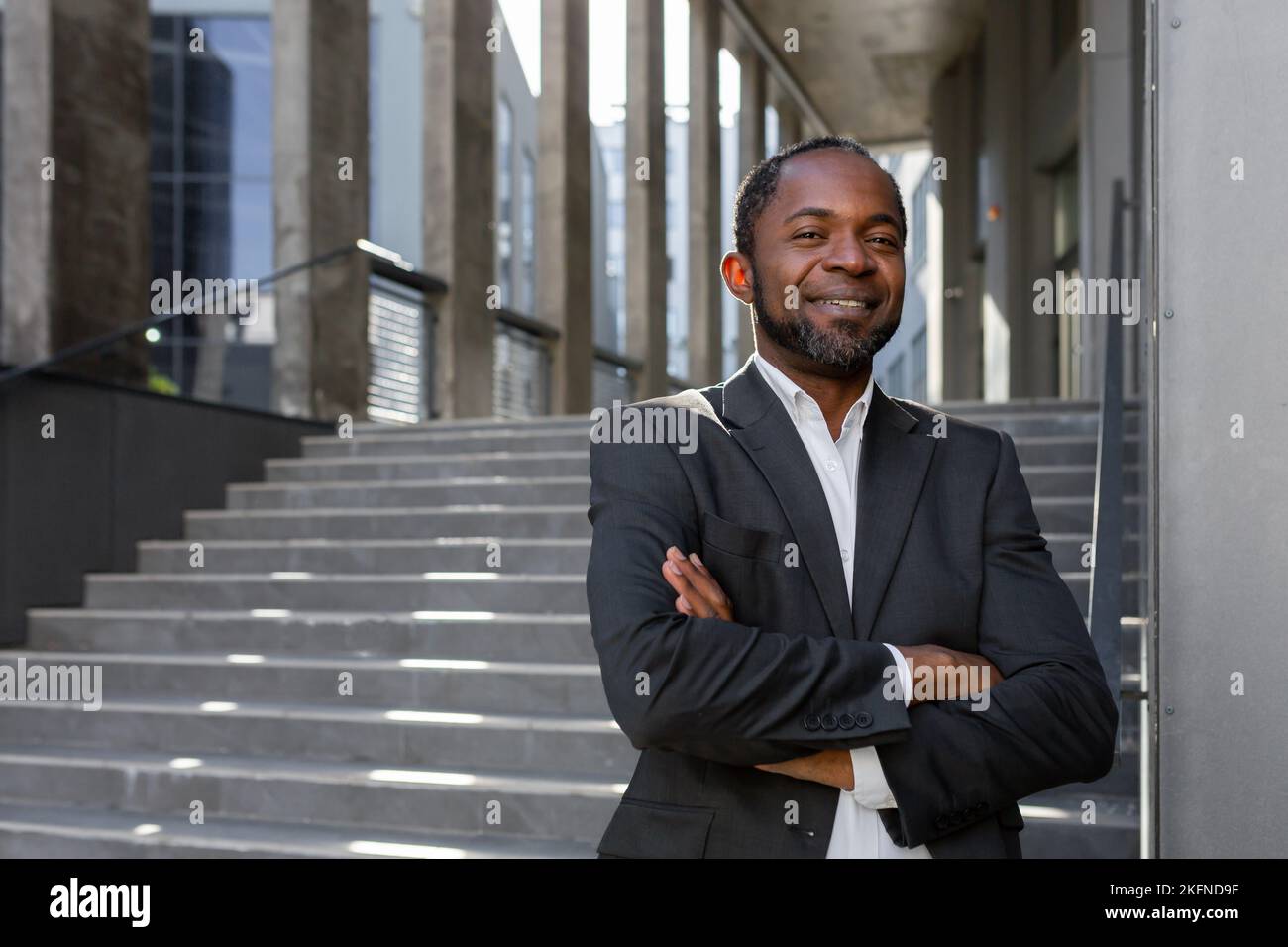 Portrait d'un homme d'affaires afro-américain couronné de succès, d'un patron mûr aux bras croisés souriant et regardant l'appareil photo, homme d'affaires senior devant le bâtiment de bureau près des escaliers. Banque D'Images