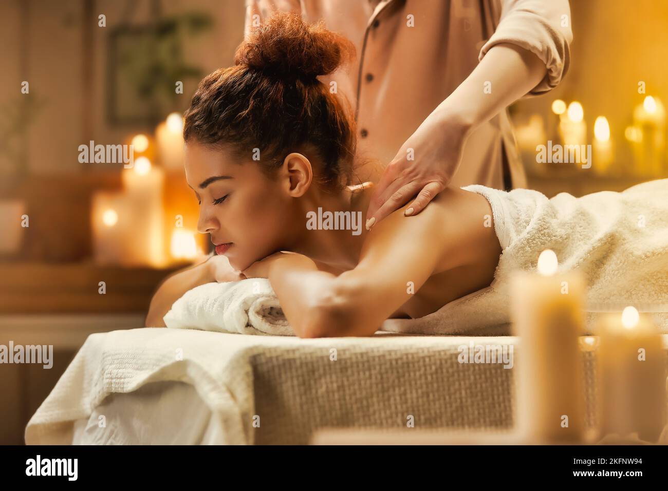 Tendre fille africaine souriante profitant d'un massage avec les yeux fermés dans le spa. Banque D'Images