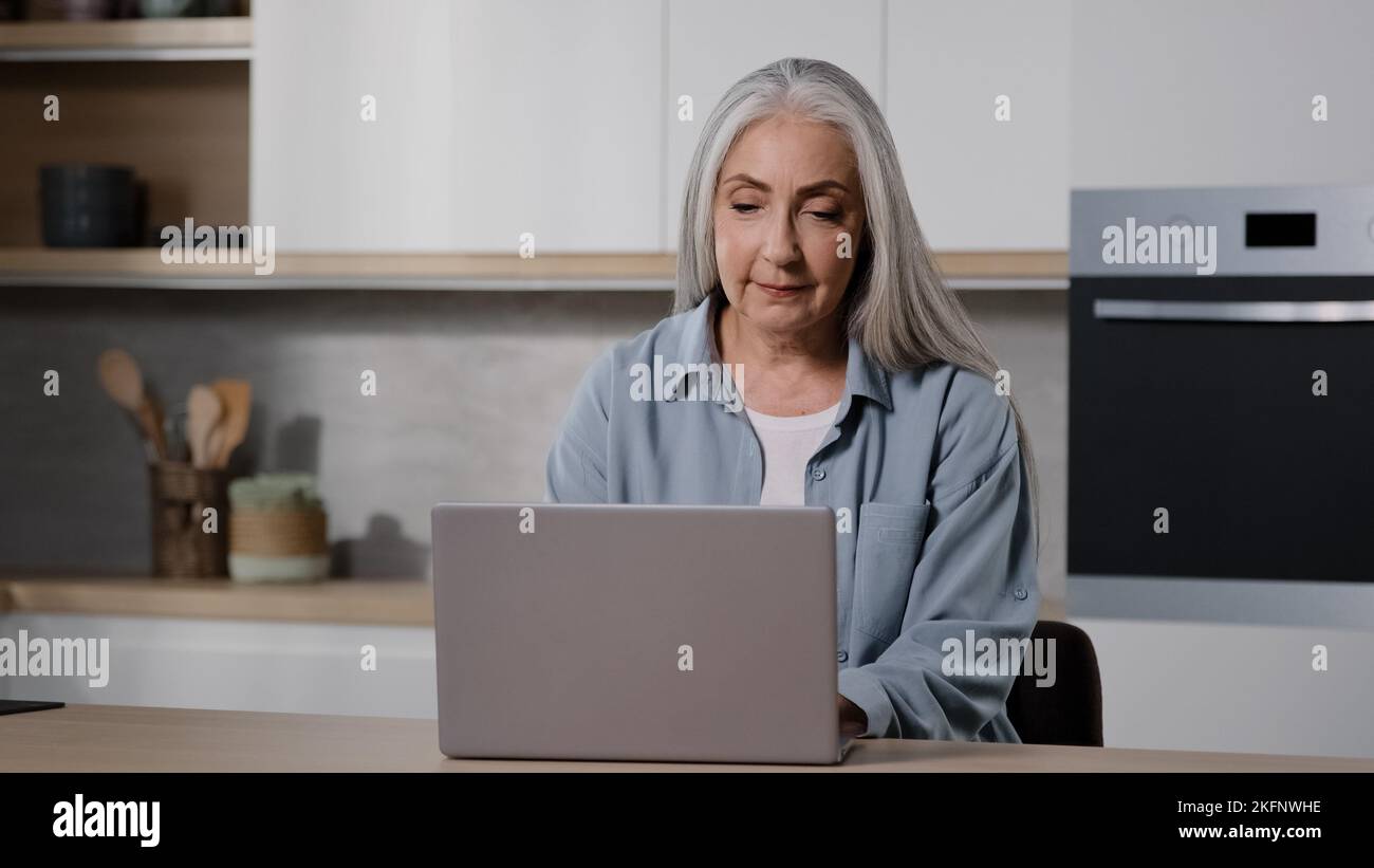 Femme d'affaires âgée femme indépendante senior travailler sur ordinateur portable à partir de la saisie à domicile sur le clavier de l'ordinateur portable chat en ligne utiliser le logiciel de navigation d'application d'ordinateur Banque D'Images
