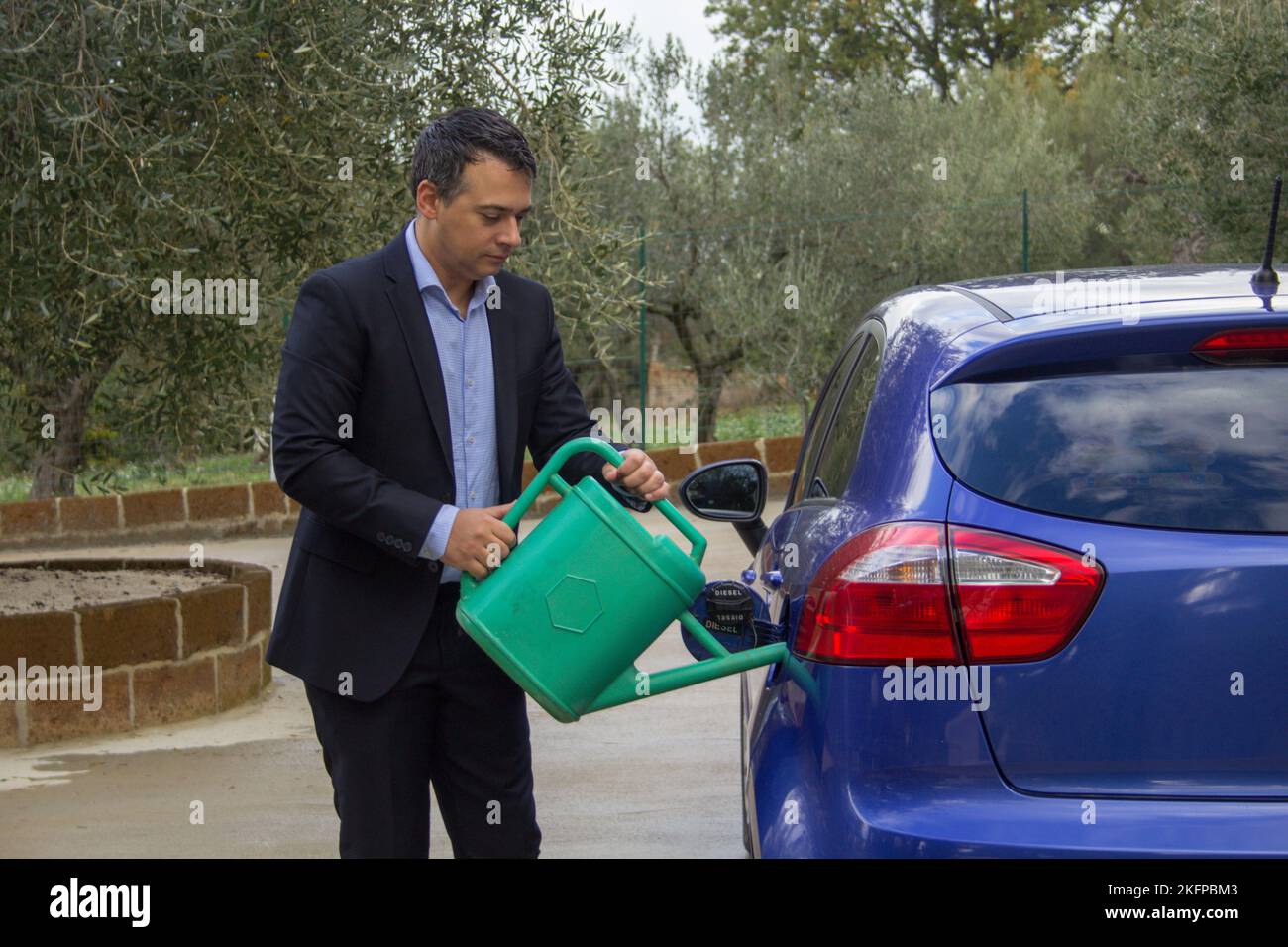 Image d'un homme élégant qui verse de l'eau dans le réservoir de voiture avec une arroseur. Référence au coût élevé du carburant et à la transition vers les voitures à hydrogène. Banque D'Images