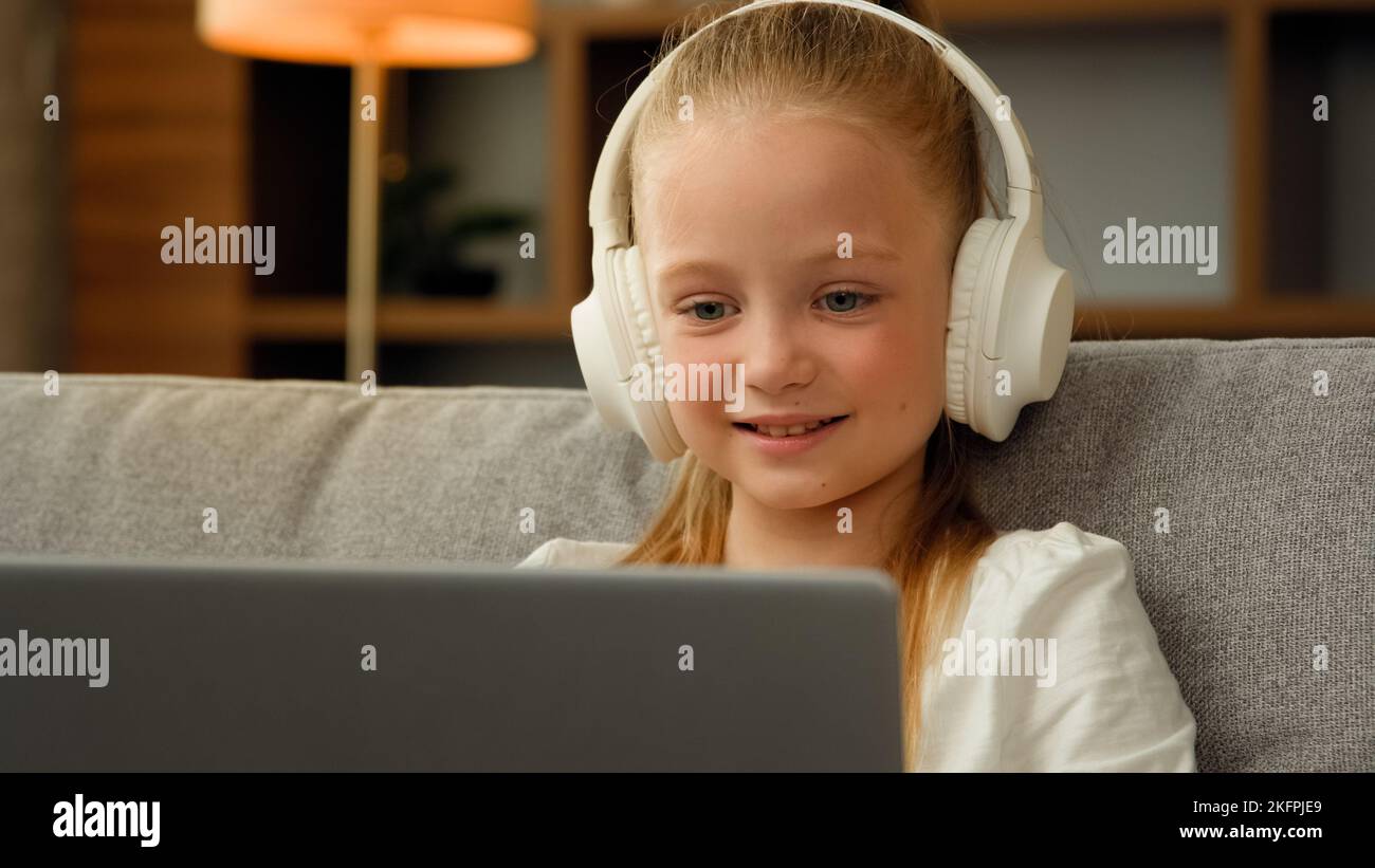 Beau enfant petit gamer étudiant en ligne sur un ordinateur portable à la maison écouter de la musique audio dans les écouteurs jouer jeu d'ordinateur rire jolie fille montre Banque D'Images