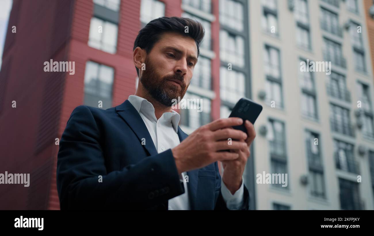 Caucasien barbu homme d'affaires entrepreneur tenir portable SMS messages stand dans la ville avec des bâtiments de bureau modernes utilisent des affaires mobiles Banque D'Images