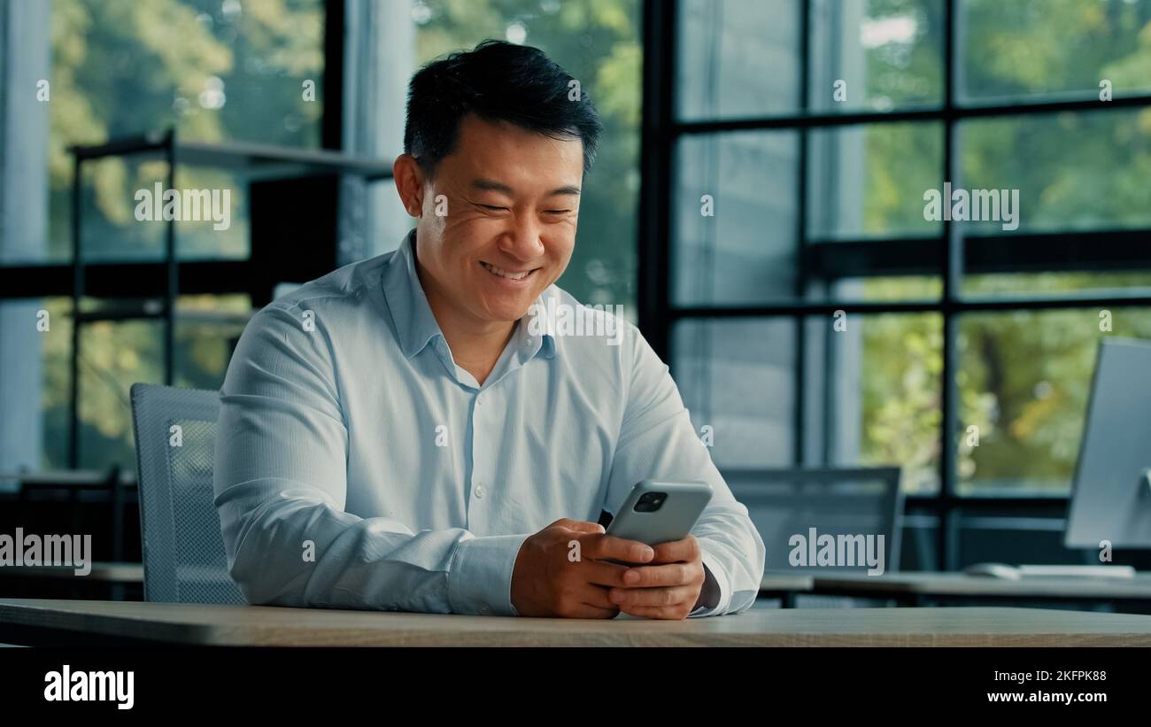 Portrait de sexe masculin asiatique chinois homme entrepreneur employeur travailler au bureau regarder moderne gadget téléphone mobile écran recherche information utilisation en ligne Banque D'Images