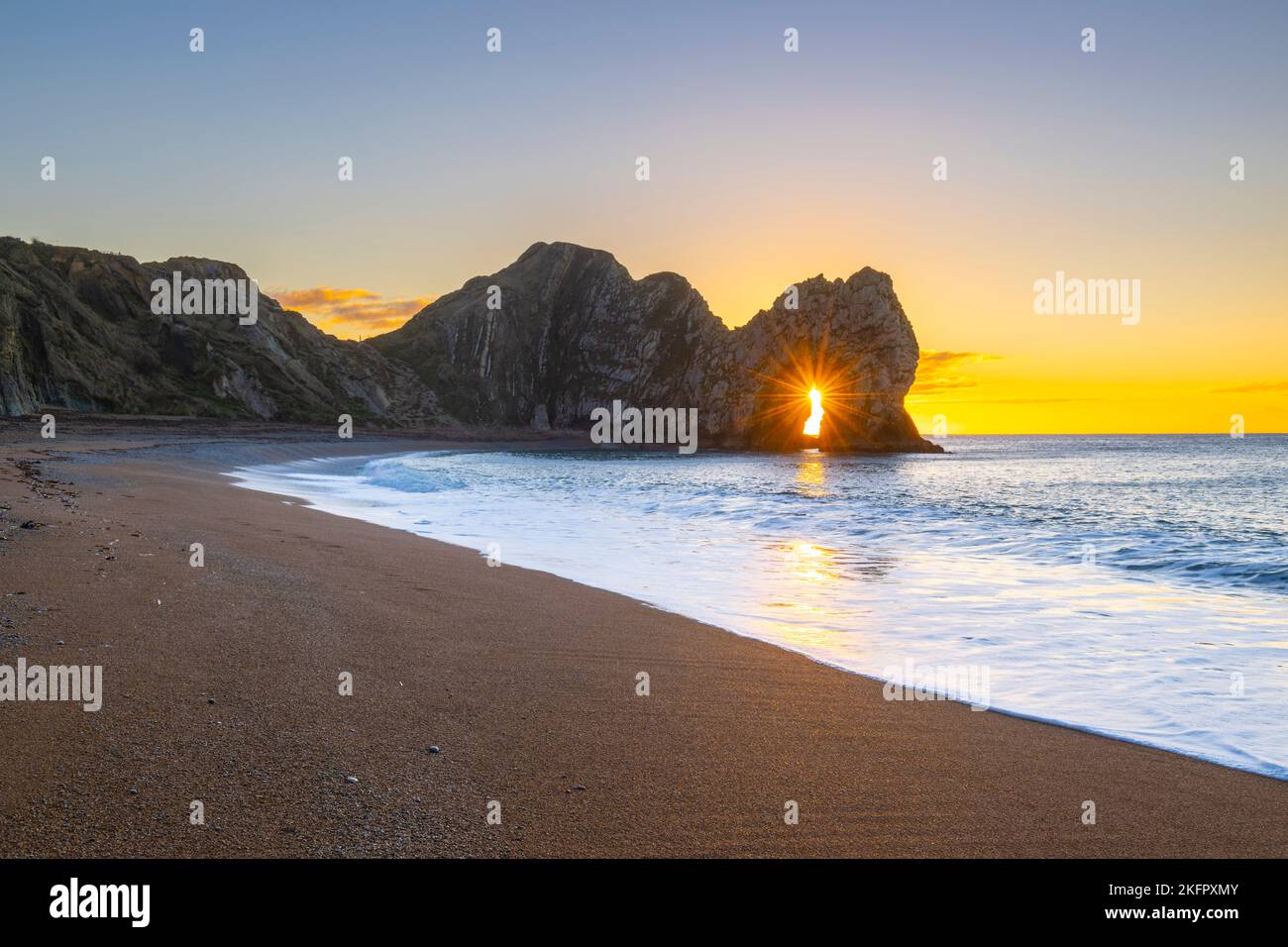 Un lever de soleil spectaculaire tandis que le soleil brille à travers le trou clé de l'arche de mer calcaire de Durdle Door sur la côte jurassique Dorset, Royaume-Uni sur un froid, clea Banque D'Images