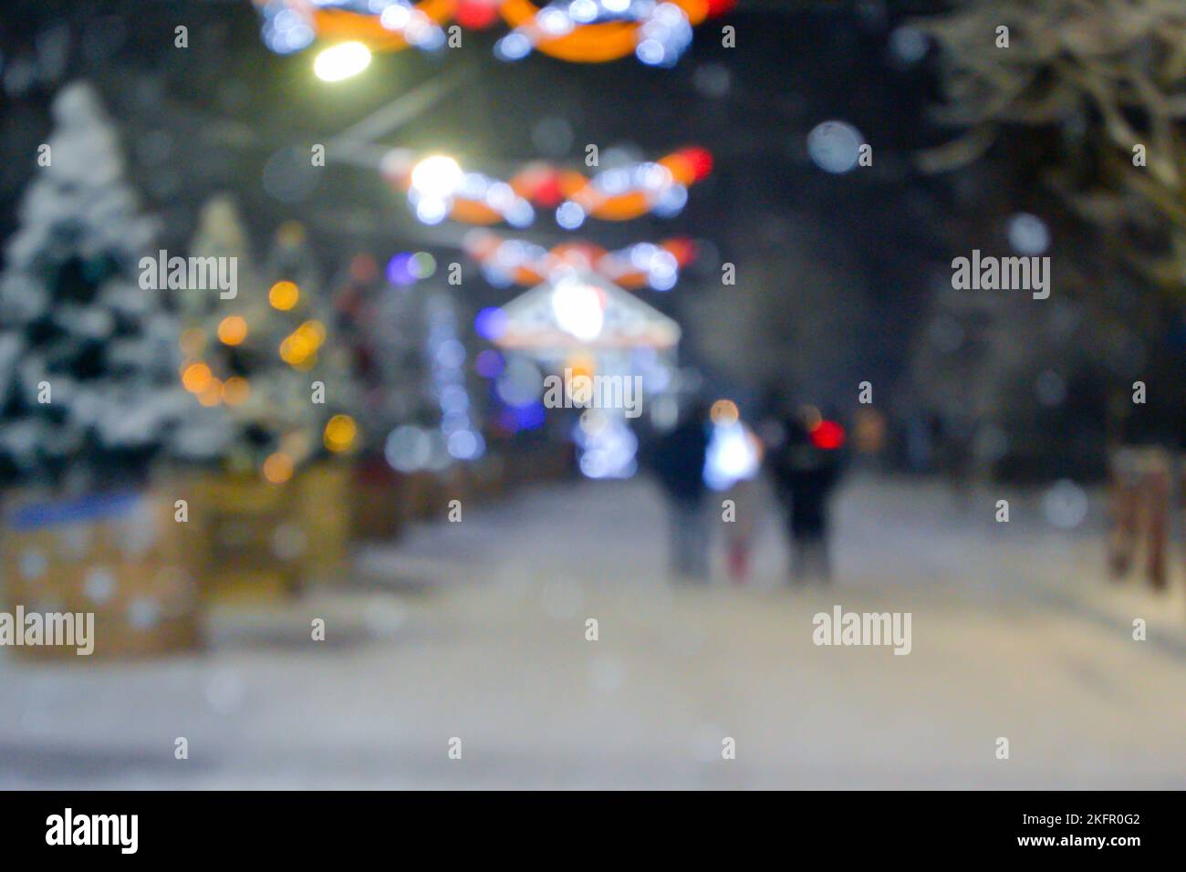 Résumé arrière-plan flou. Personnes marchant dans la rue d'arbres de Noël décorés décorés avec éclairage lumineux, lumières lumineuses et guirlandes dans la ville pendant de fortes chutes de neige la nuit d'hiver Banque D'Images