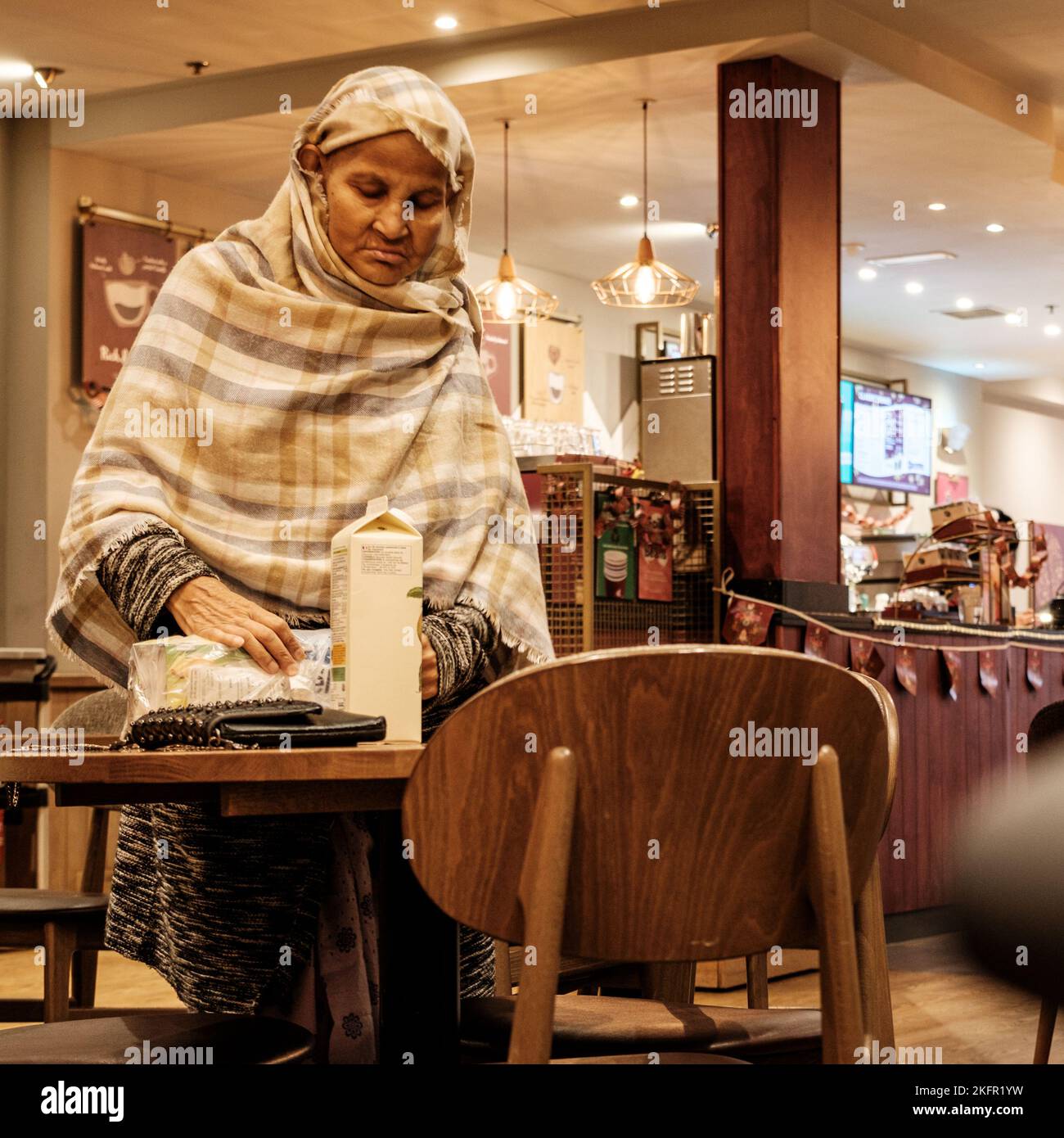 Epsom, Surrey, Londres, Royaume-Uni, 19 novembre 2022, femme âgée musulmane islamique en robe traditionnelle et tête couvrant dans Un café de rue Banque D'Images