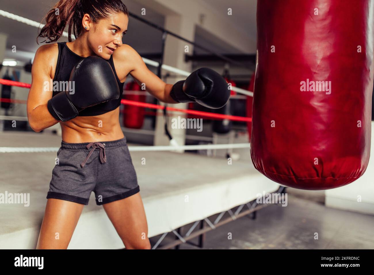 Boxeur sportif féminin s'entraîner avec un sac de poinçonnage dans une salle de fitness. Jeune femme sportive pratiquant ses techniques de poinçonnage dans un gymnase de boxe. Banque D'Images