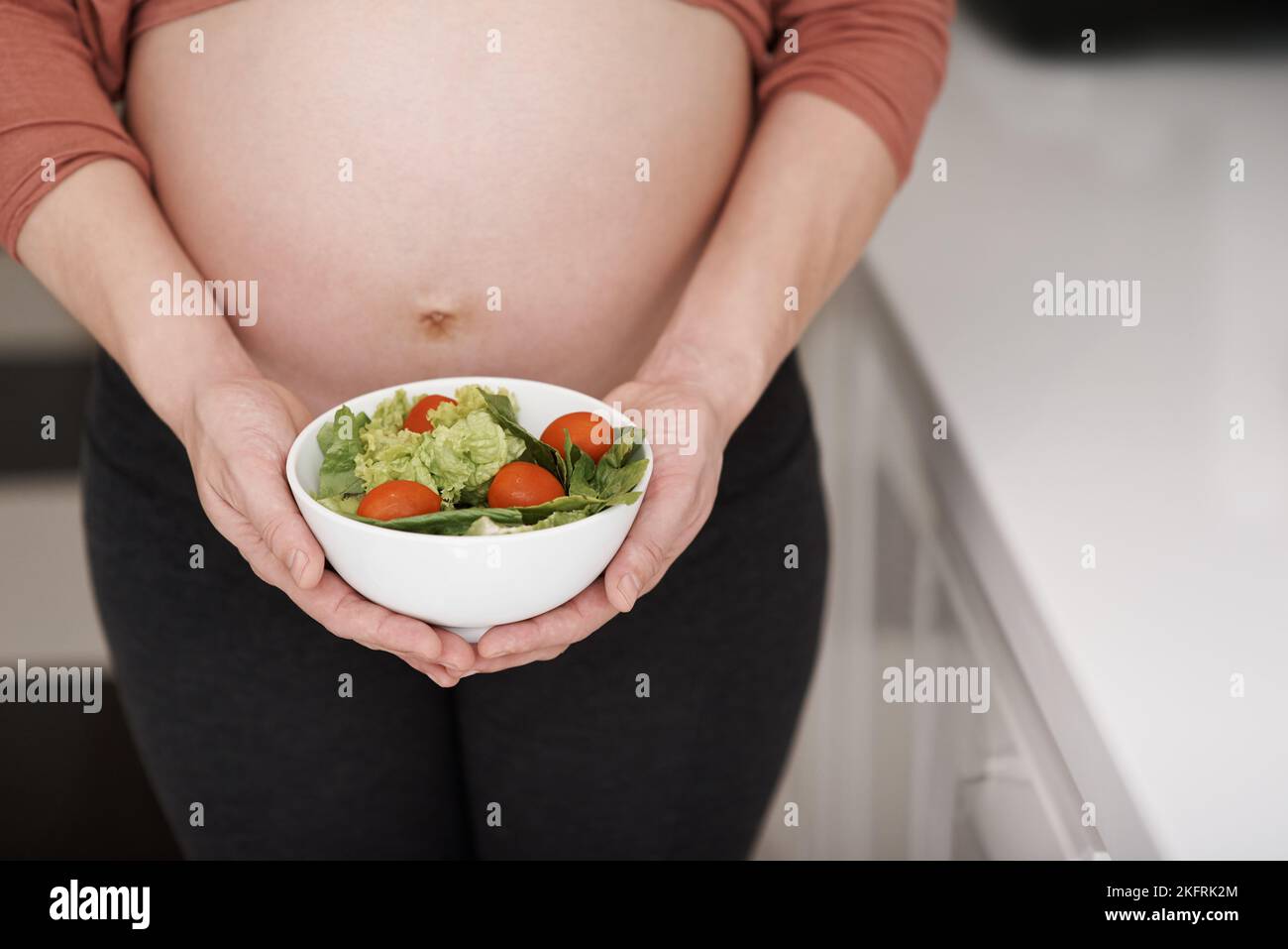 Le meilleur choix pour la femme enceinte. Une jeune femme enceinte tenant une salade dans la cuisine. Banque D'Images