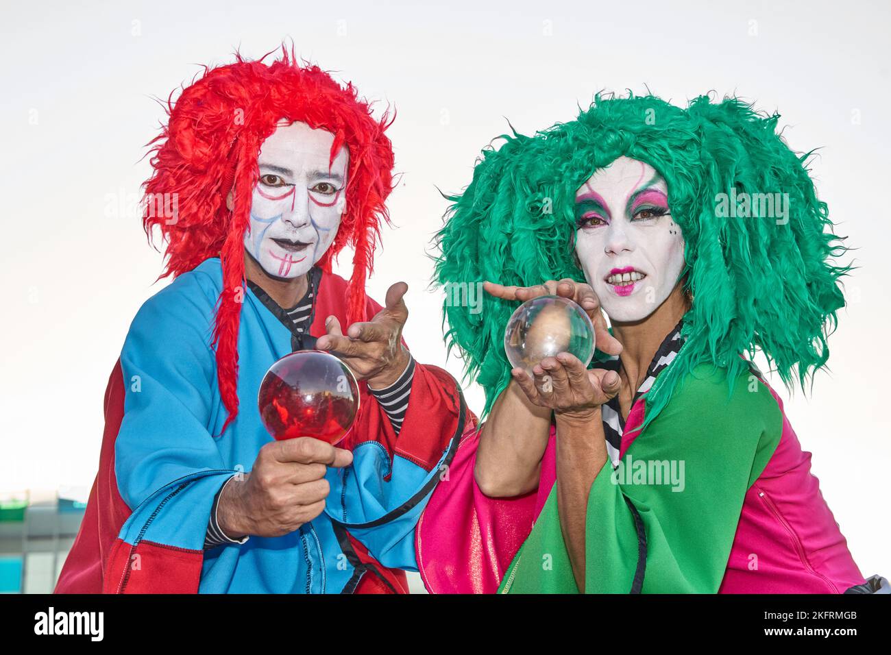 Clowns masculins et féminins en costumes et perruques colorés, regardant la caméra tenant des boules de cristal dans leurs mains. Banque D'Images