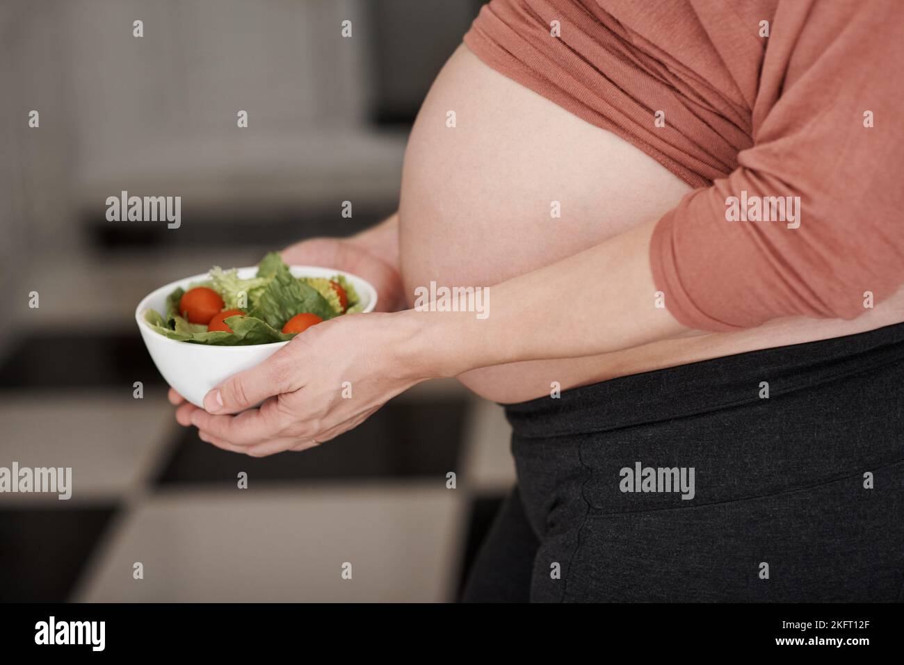 Une petite femme enceinte qui tient une salade dans la cuisine. Banque D'Images