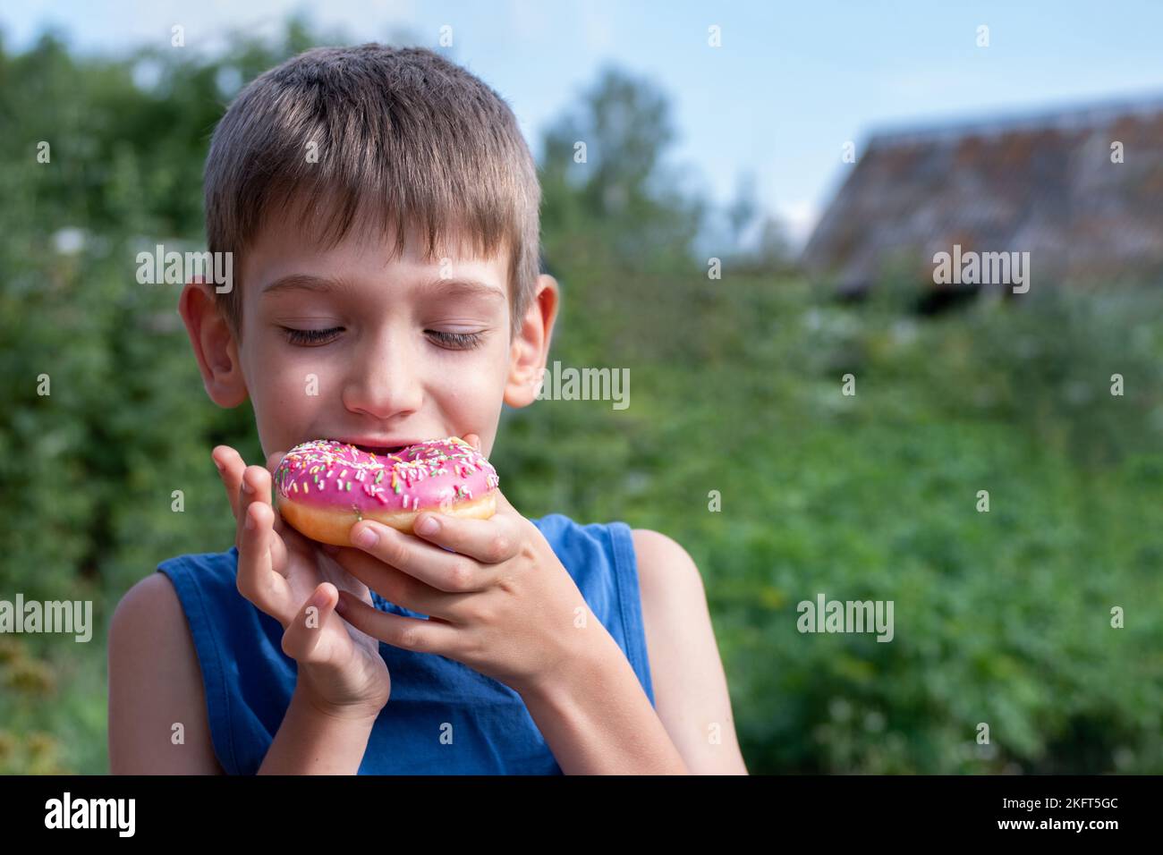 Un enfant heureux mange un beignet rose dans le parc. L'enfant refuse de manger des aliments sains. Concept alimentaire malsain, grignotage de nourriture douce. Les enfants adorent swee Banque D'Images