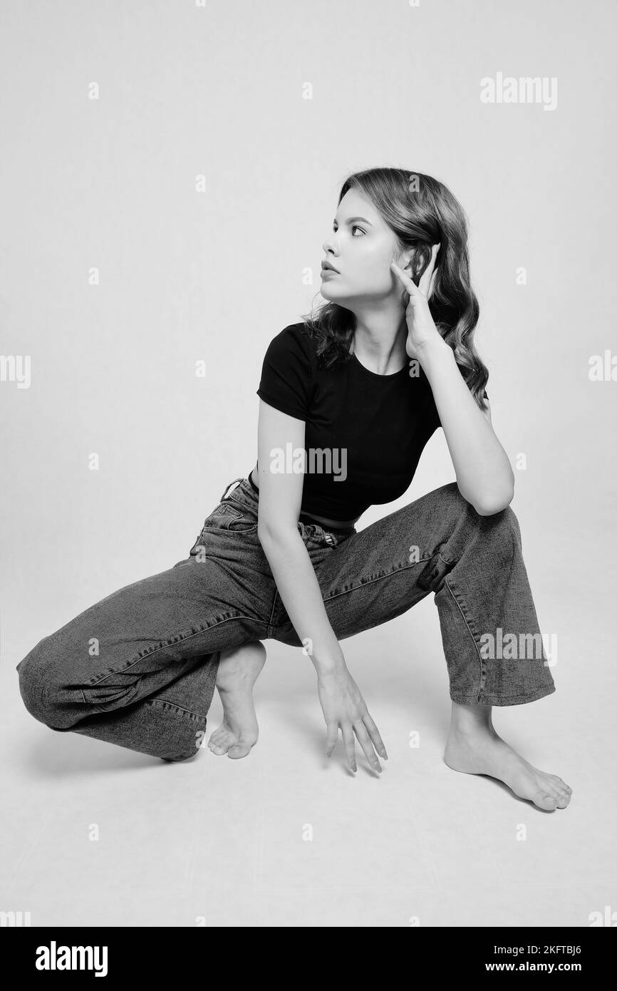 Portrait de la belle femme moderne en chemise noire et jeans pose sur fond blanc monochrome Banque D'Images