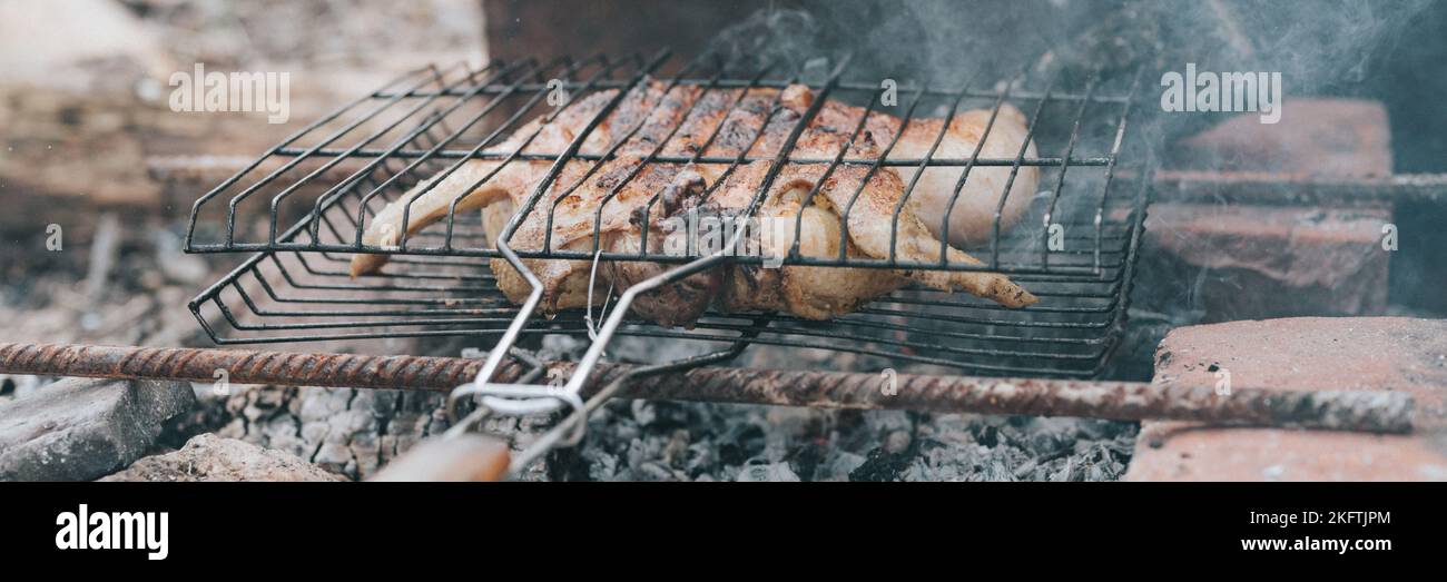 les aliments à base de viande de poulet sont frits sur le gril sur des charbons couvants ou ember du feu de camp sur terre les jours d'été ou d'automne. barbecue en conditions de camping. sur Banque D'Images