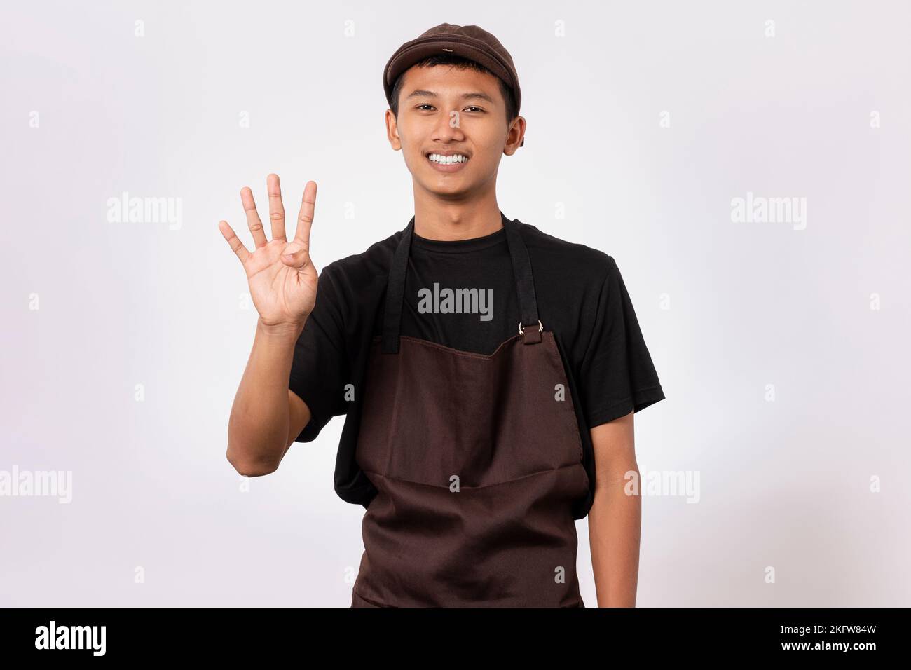 Beau barista asiatique homme portant un tablier marron et un t-shirt noir isolé sur fond blanc faisant un geste de chiffre avec les doigts Banque D'Images