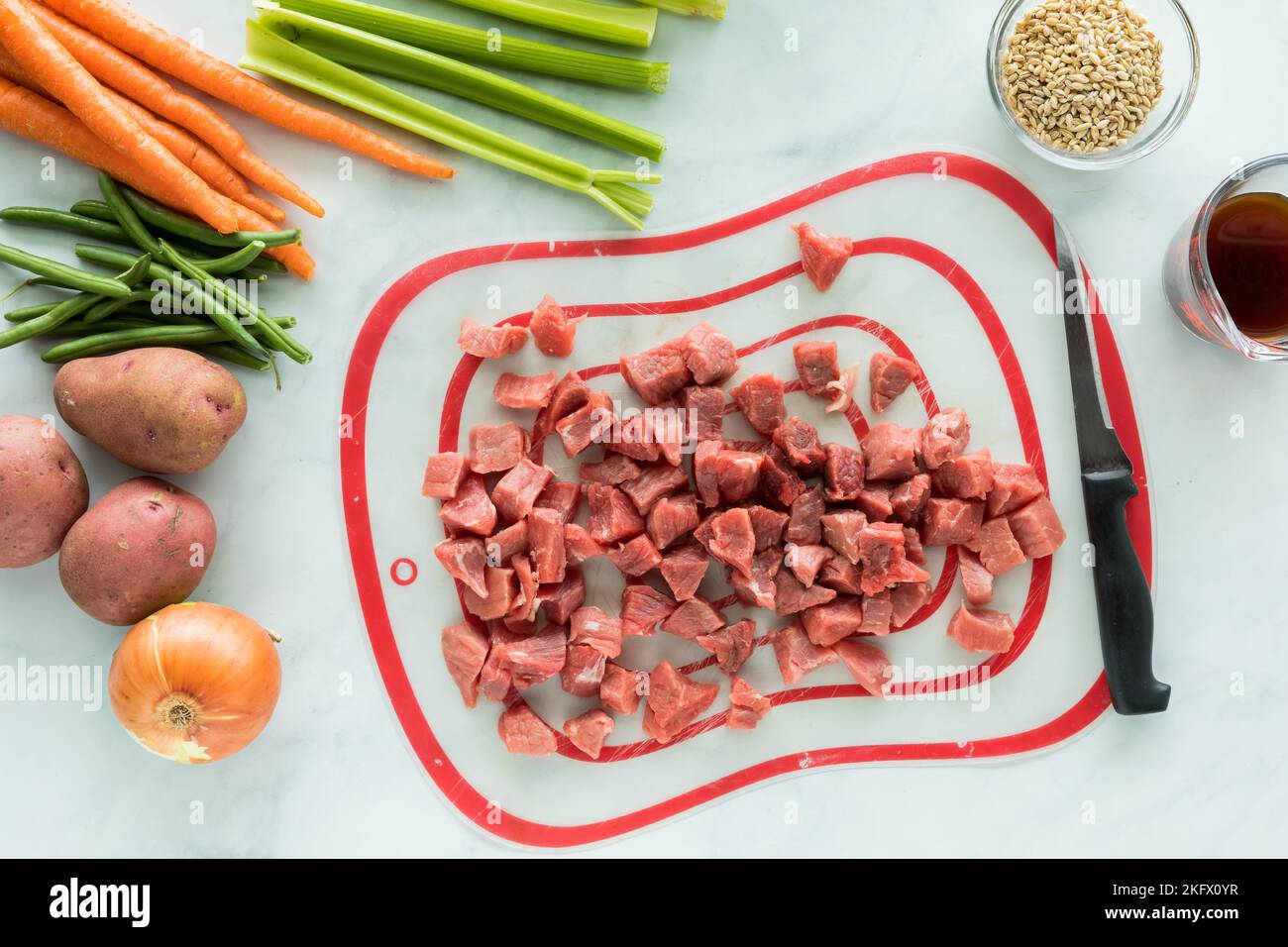 Vue de dessus en bas des morceaux de bœuf ratés sur un tapis de découpe avec des légumes sur le côté. Banque D'Images
