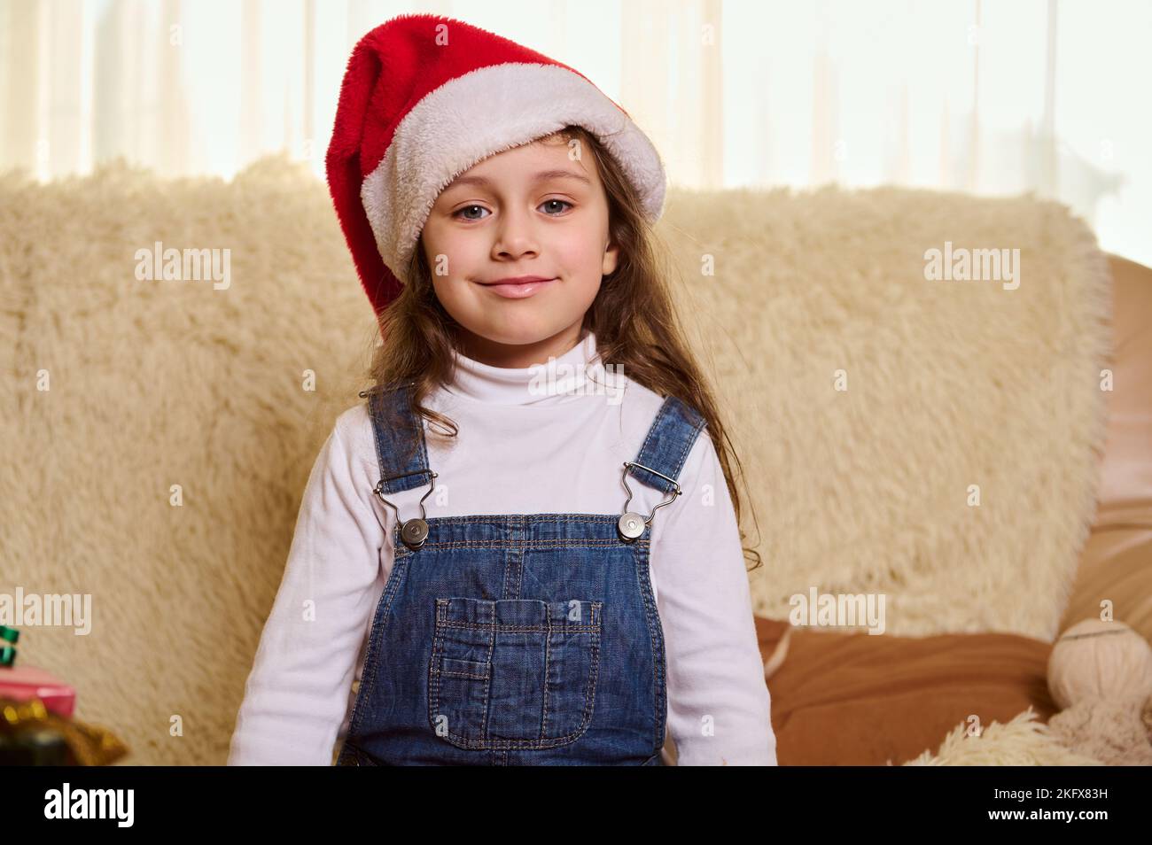 Portrait en gros plan d'une belle petite fille caucasienne portant un chapeau de père Noël, souriant et regardant l'appareil photo. Noël Banque D'Images