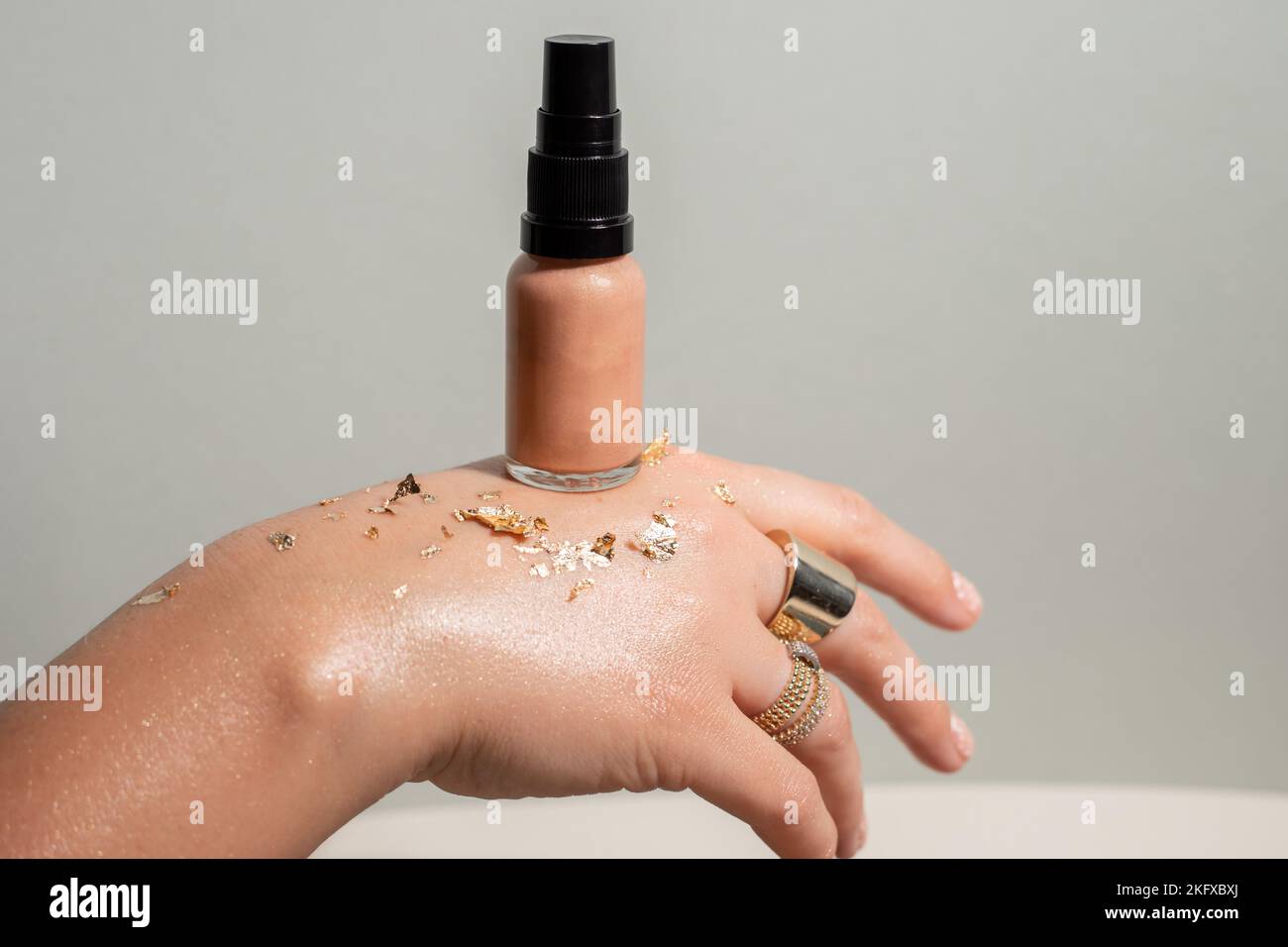 Femme méconnaissable main avec des anneaux, des sparkles dorés, tinsel présent beige naturel maquillage crème de fondation correcteur Banque D'Images