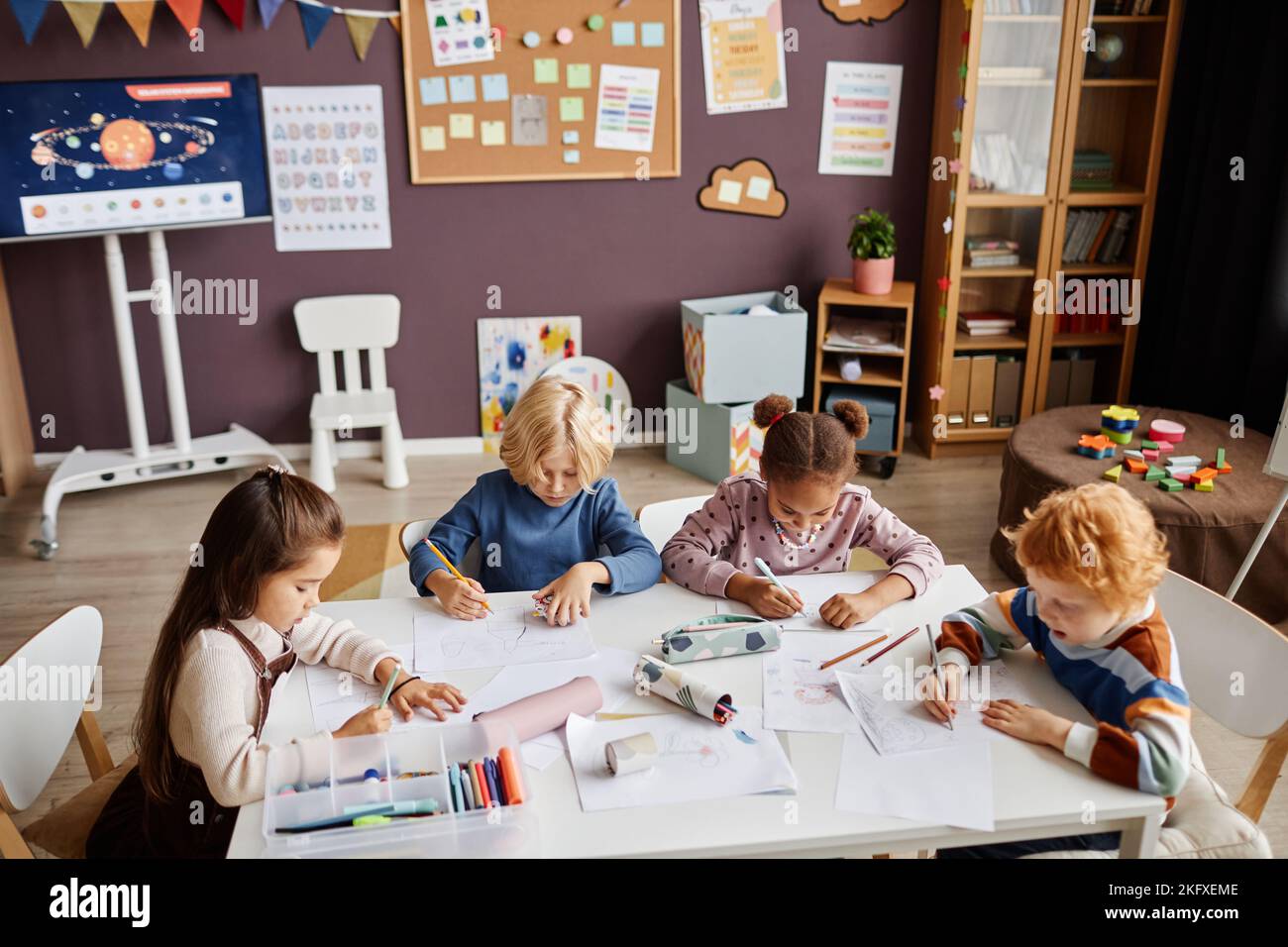 Groupe de petits apprenants créatifs de l'école maternelle réunis par le dessin de table avec des crayons multicolores à la leçon des arts en classe Banque D'Images